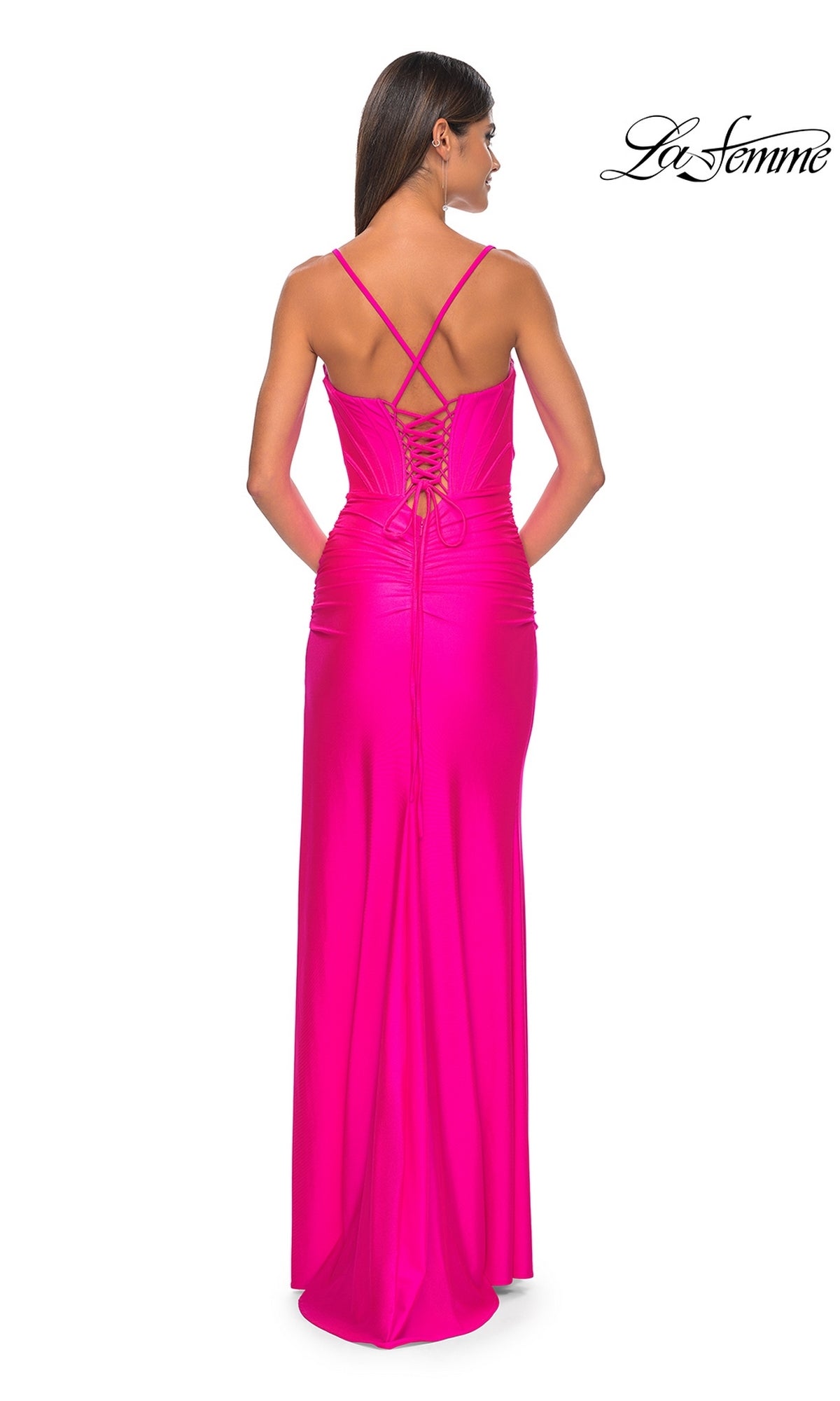 Woman in a bright pink La Femme Long Bustier-Bodice Prom Dress 32256, featuring crisscross straps, corset-style bodice, and lace-up back, stands facing away from the camera.